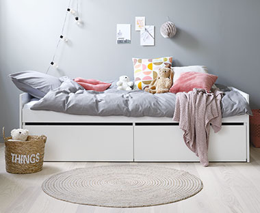 Біле односпальне дитяче ліжко з сірою постіллю та кольоровими подушками