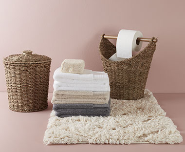 Білий килимок для ванної кімнати, складені рушники та плетений кошик